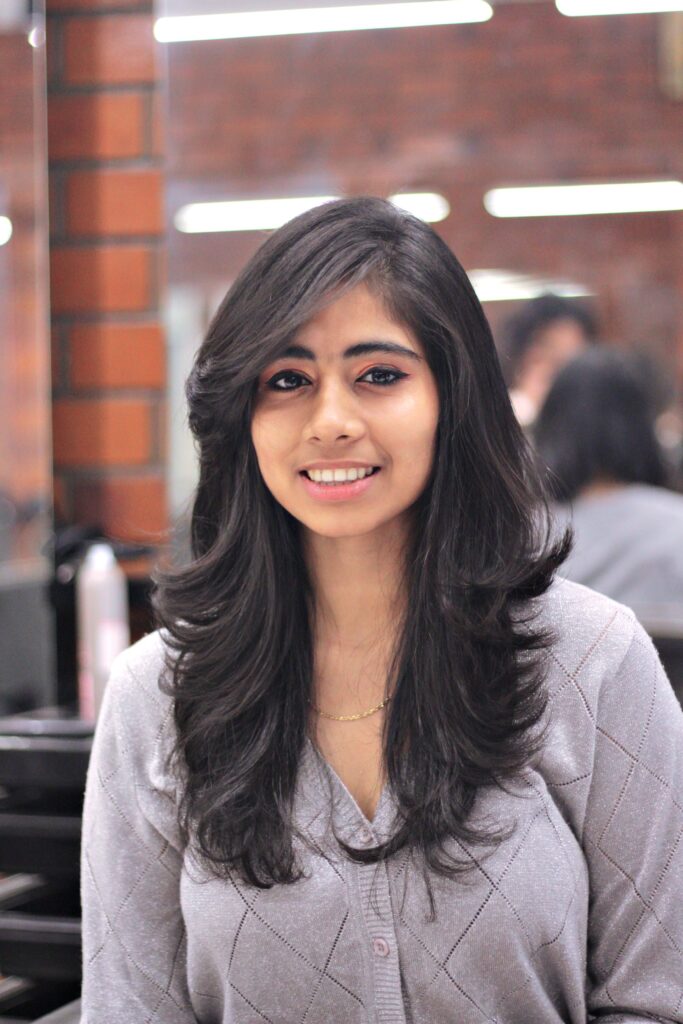 Portrait of a smiling woman with long hair in a modern salon setting, exuding confidence and style.