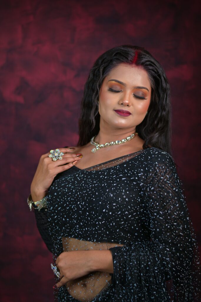 Beautiful portrait of a woman in a sparkling black saree with jewelry, set against a rich backdrop.