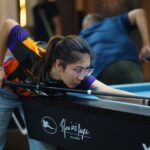 Female player intently aiming a shot during a billiards game indoors.
