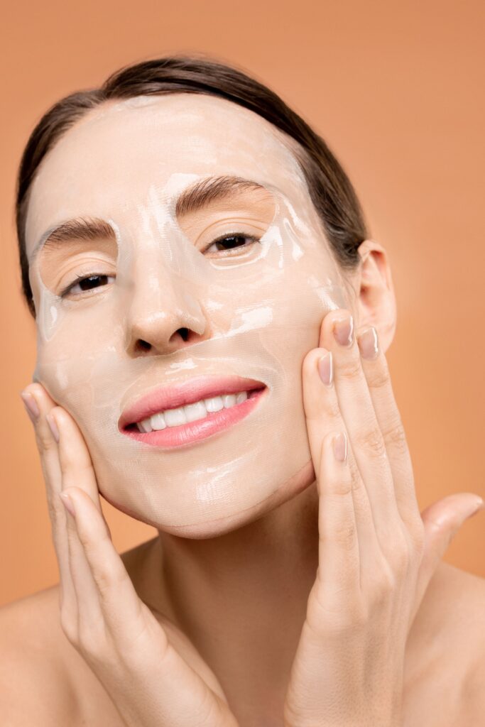 Close-up of a woman applying a clear moisturizing face mask with a smile.